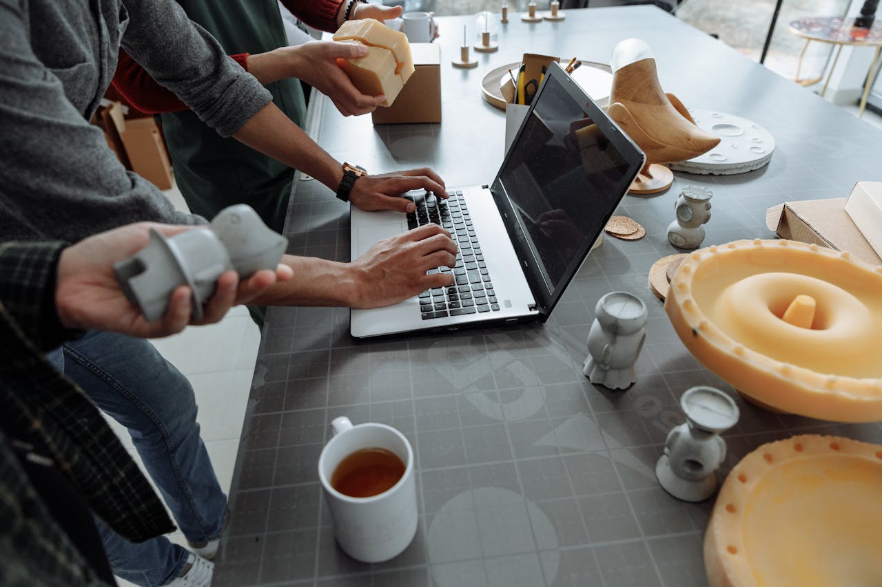 Hands on laptop in a creative workspace with 3D models and prototypes.